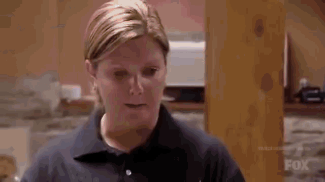 a woman is standing in a kitchen wearing a blue shirt and looking at the camera .