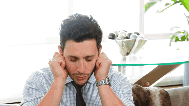 a man in a plaid shirt and tie covering his ears