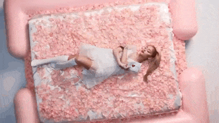 a woman is laying on her stomach in a pile of pink petals holding a letter with a heart on it .