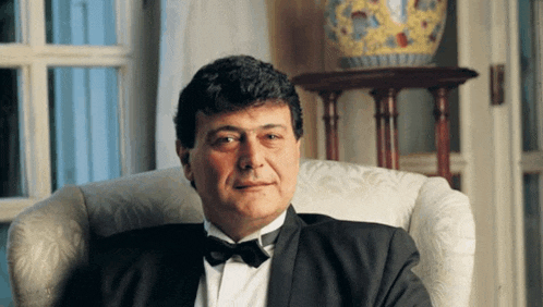a man in a tuxedo sits in a chair