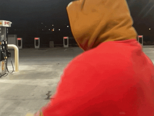 a person wearing a red hoodie stands in front of a gas pump