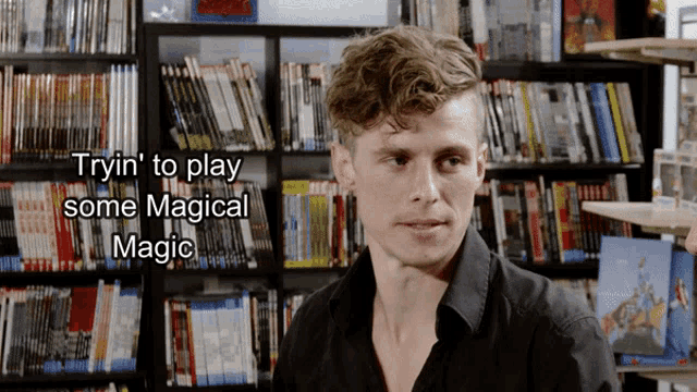 a man in a black shirt stands in front of a bookshelf with the words tryin ' to play some magical magic above him