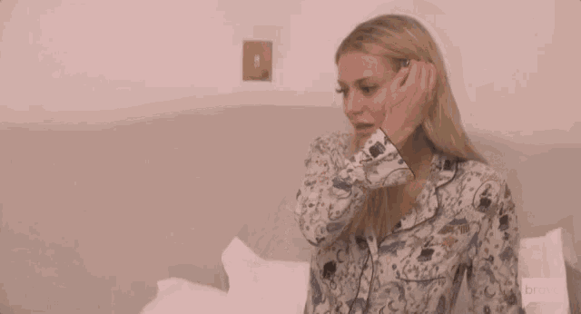 a woman is sitting on a bed with a bravo logo on the bottom right