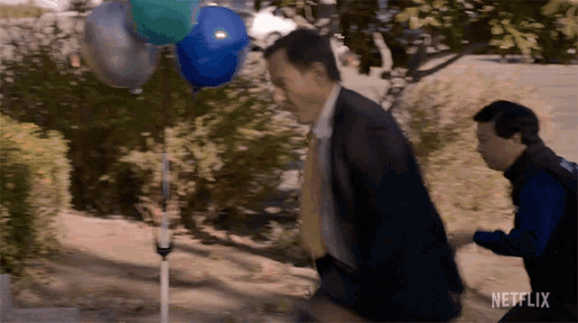 a man in a suit is running towards a bunch of balloons
