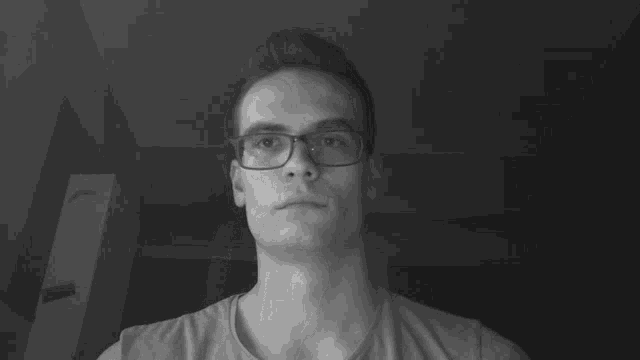 a black and white photo of a man wearing glasses and a grey shirt