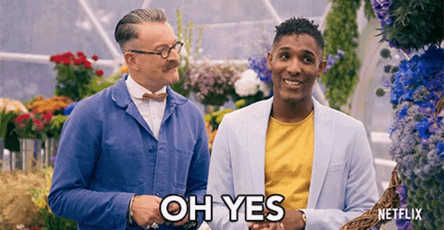 two men are standing next to each other in front of flowers and one of them is saying oh yes
