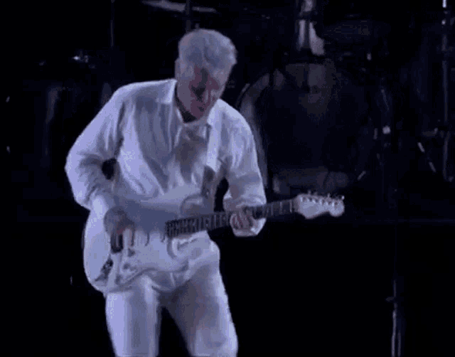 a man in a white shirt is playing a white guitar on a stage .