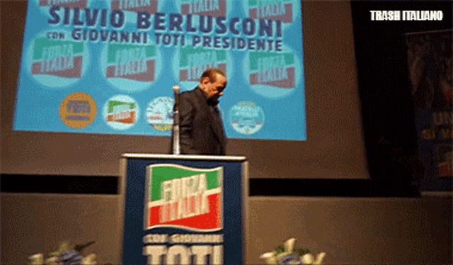 a man stands at a podium in front of a sign that says silvio berlusconi con giovanni toti presidente
