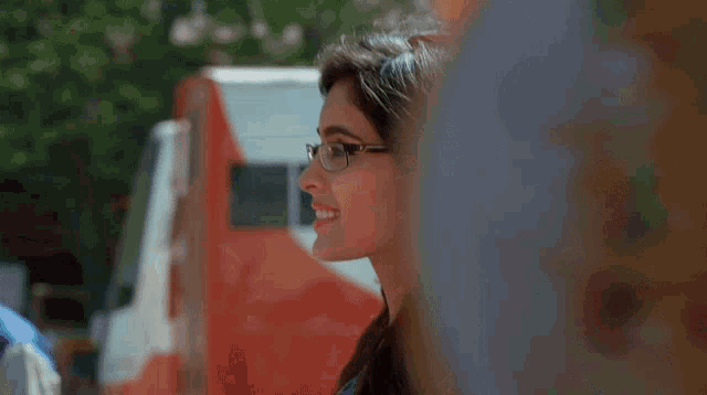 a woman wearing glasses and earrings smiles in front of a red and white truck