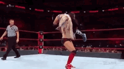 a wrestler is kicking another wrestler in the face while a referee watches .