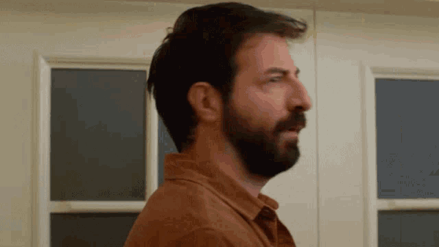 a man with a beard is standing in front of a window with his mouth open .