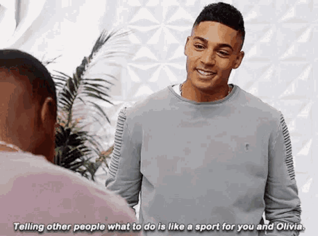 a man is talking to another man while wearing a grey sweater .