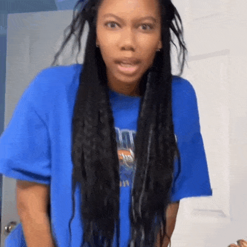 a woman with long braids is wearing a blue t-shirt and making a funny face .
