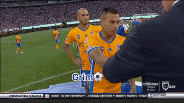 a man in a suit talks to a soccer player named grimo