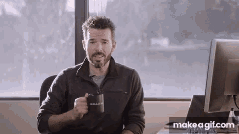 a man is sitting at a desk holding a mug that says bullet
