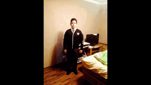 a boy in a black sweater and tie stands in front of a computer desk