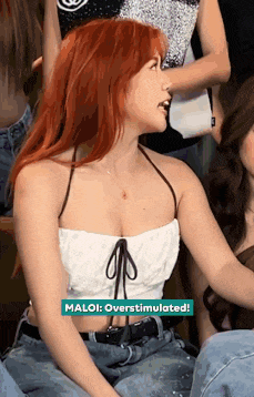 a woman with red hair is wearing a white crop top and blue jeans .