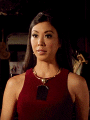 a woman wearing a red tank top and a necklace looks at the camera