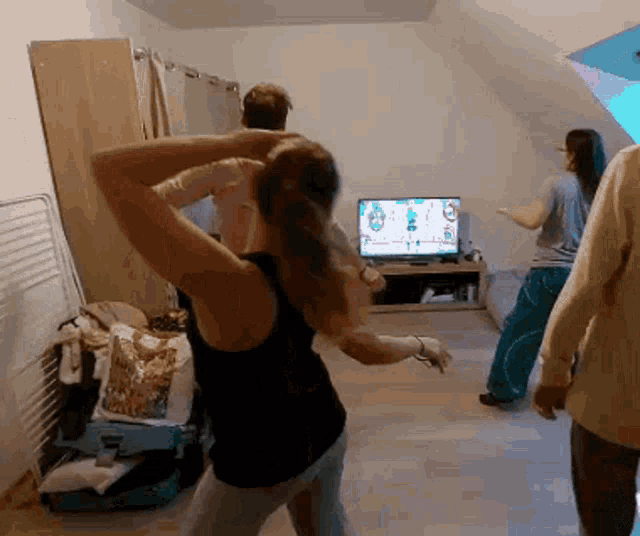a woman in a black tank top is dancing in front of a television with a game on it