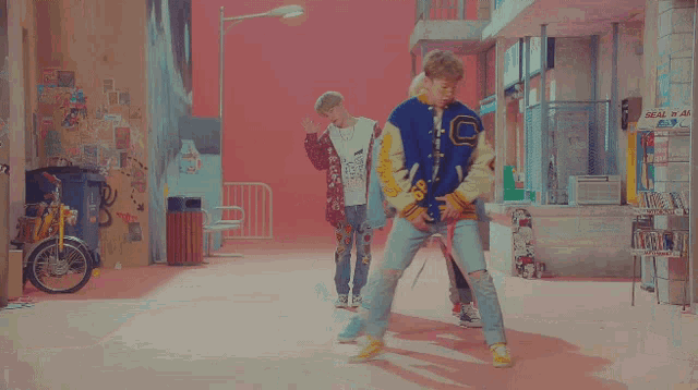 a man wearing a varsity jacket with the letter c on it is standing next to another man