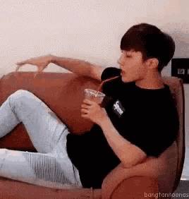 a young man is sitting on a couch holding a glass of water .