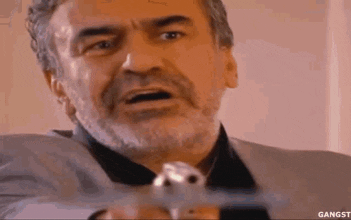 a man with a beard is holding a gun to his face .