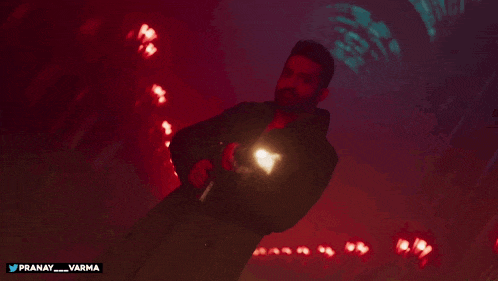 a man in a black jacket is holding a gun with the hashtag pranay_varma below him