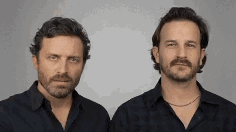two men with beard and mustache are standing next to each other .