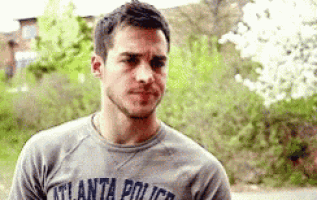 a man wearing a gray atlanta police t-shirt is standing in front of trees .
