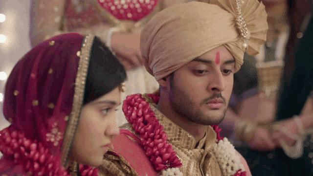 a bride and groom are sitting next to each other and the bride is wearing a red veil