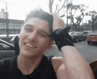 a young man wearing a bandana on his wrist is smiling and holding his head .