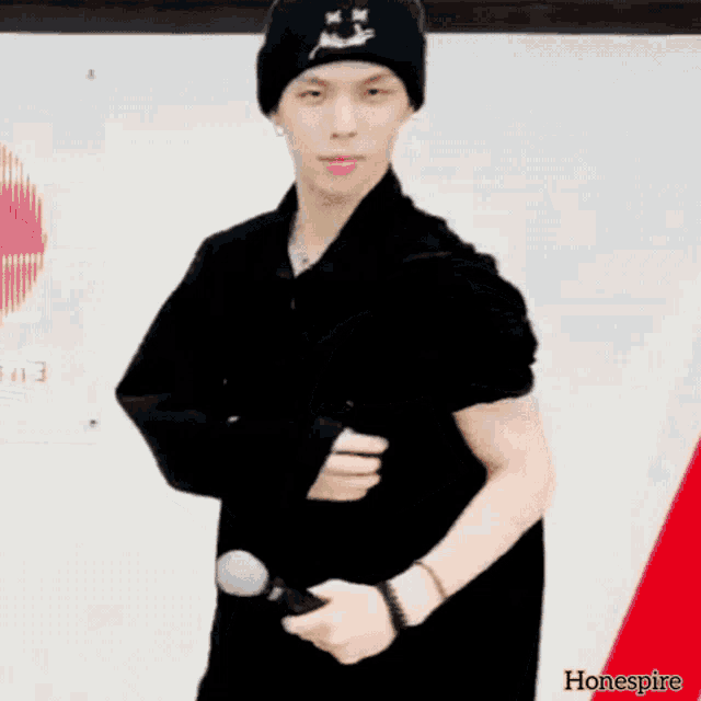 a man wearing a black beanie is holding a microphone in his right hand