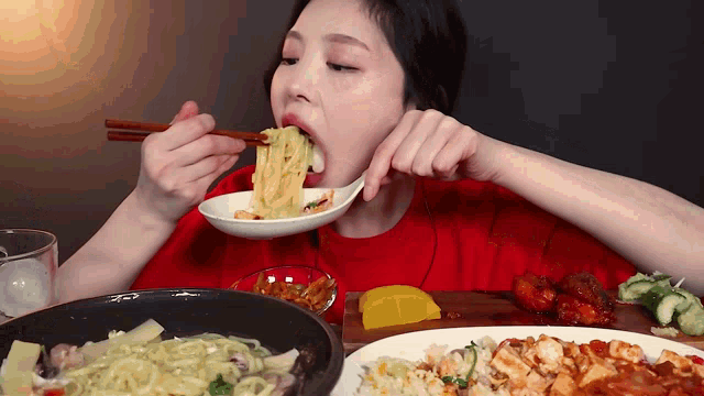 a woman in a red shirt is eating noodles from a bowl with chopsticks