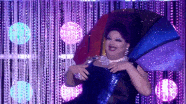 a drag queen is dancing on a stage with purple lights behind her .