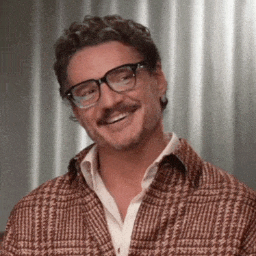 a man wearing glasses and a plaid jacket smiles for the camera