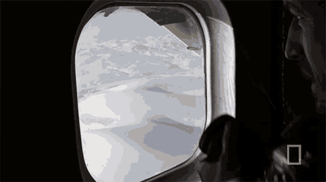 a man looking out of an airplane window with a national geographic logo on the bottom right