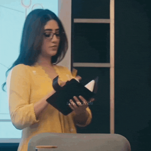 a woman in a yellow shirt and glasses is holding a notebook in her hands .