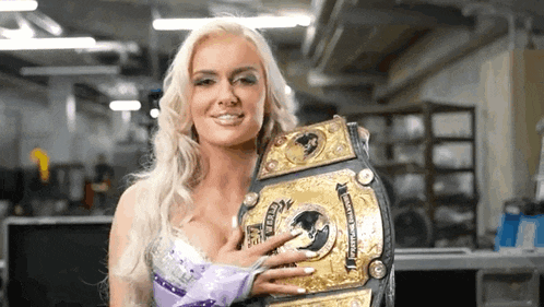 a blonde woman is holding a championship belt in her hands .