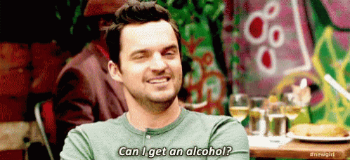 a man is sitting at a table with his arms crossed and smiling while asking can i get an alcohol .