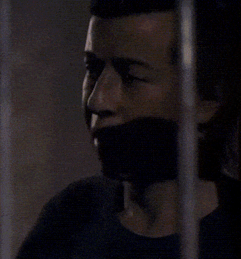 a man in a black shirt is behind bars in a jail cell