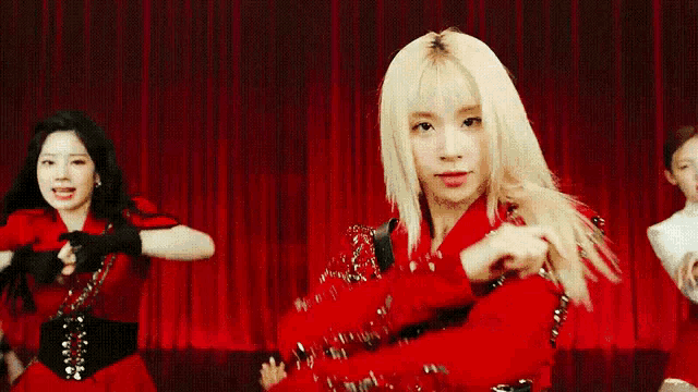 a group of women are dancing on a stage with red curtains behind them .