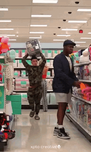 a man in a camouflage uniform is carrying a box over his head while another man looks on