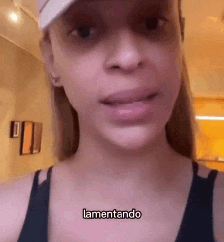 a woman wearing a hat and a black tank top is making a funny face and says lamentando .