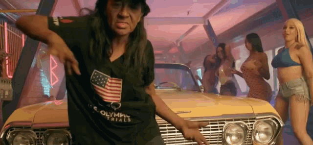 a man in a black shirt with an american flag on it is dancing in front of a yellow car .