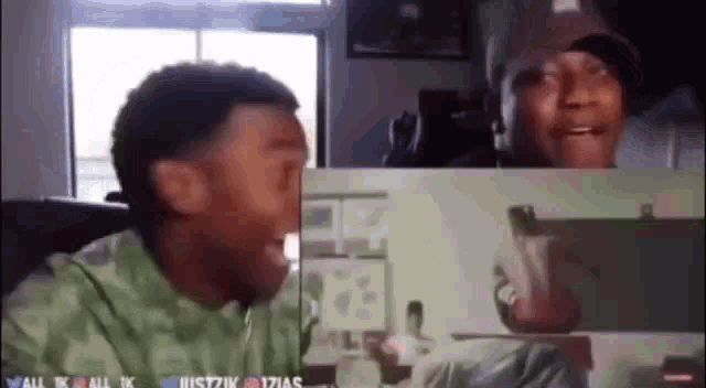 a man is laughing while looking at another man 's face on a computer screen .