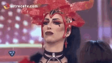 a drag queen is wearing a red costume and a choker .
