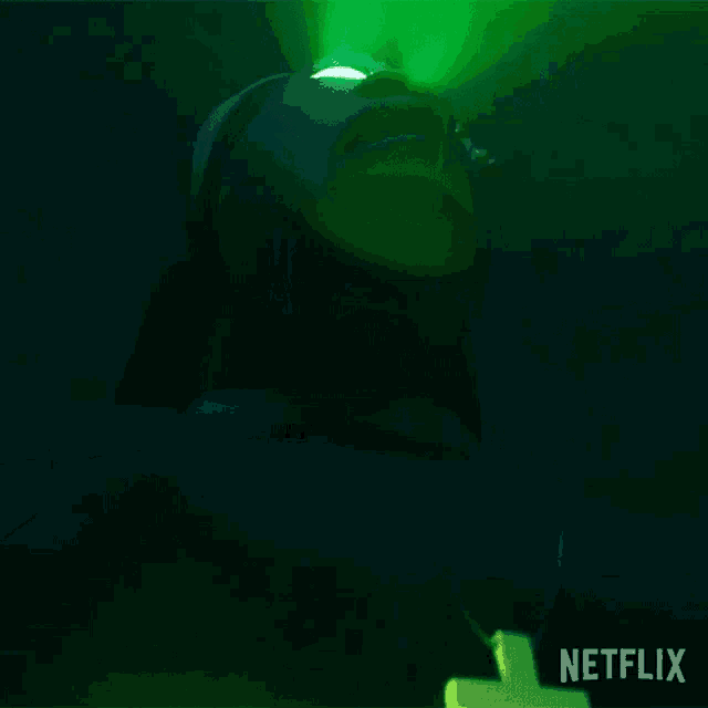 a man with a cross on his chest looks up at a green light that is coming from netflix
