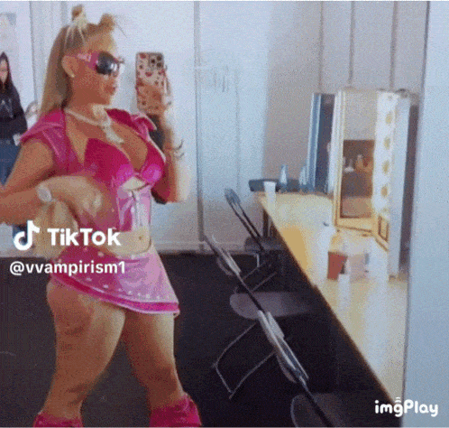 a woman in a pink outfit is taking a picture of herself in a dressing room