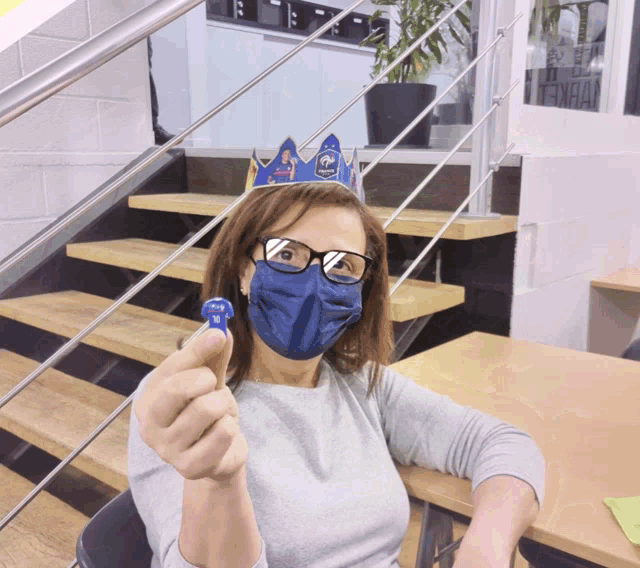 a woman wearing a blue mask and a crown holds up a blue object