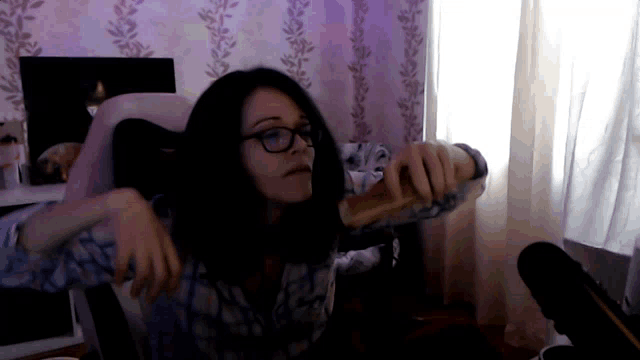 a woman wearing glasses holds a hot dog in front of a window